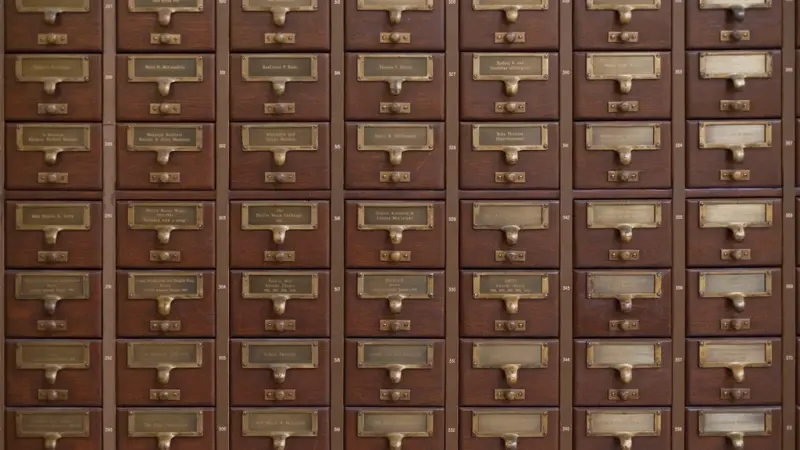 Rows of wooden library card catalog drawers with small brass handles and paper labels